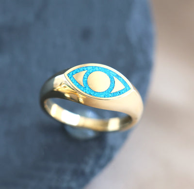 Gold signet ring with blue eye and black spinel inlay, unisex design in various metals.