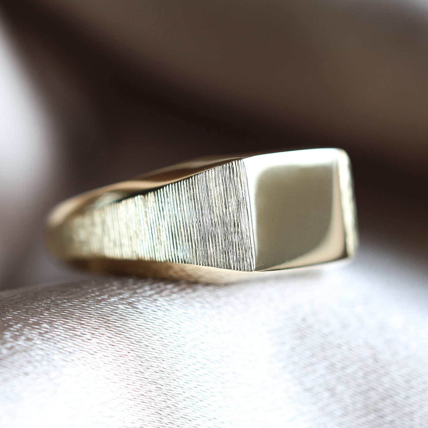 Gold signet ring on fabric surface, close-up of metal object, customizable with gemstones.