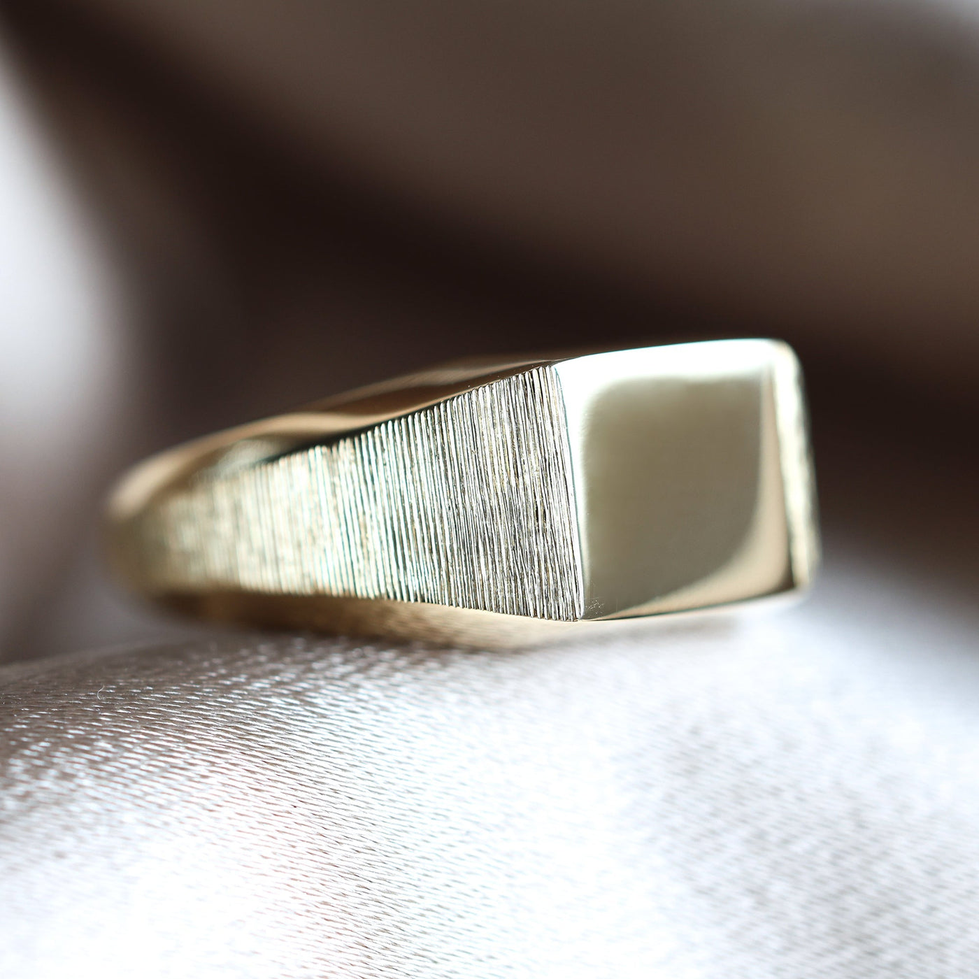 Gold signet ring on fabric surface, close-up of metal object, customizable with gemstones.