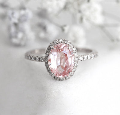 Oval-shaped peach sapphire ring with diamond halo