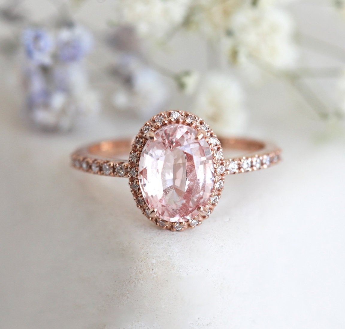 Oval-shaped peach sapphire ring with diamond halo