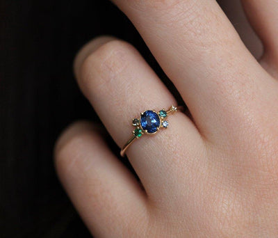 Blue oval sapphire ring with cluster diamonds and emeralds