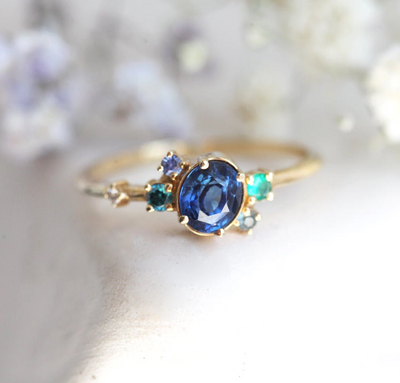 Blue oval sapphire ring with cluster diamonds and emeralds