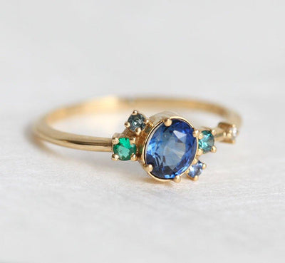 Blue oval sapphire ring with cluster diamonds and emeralds