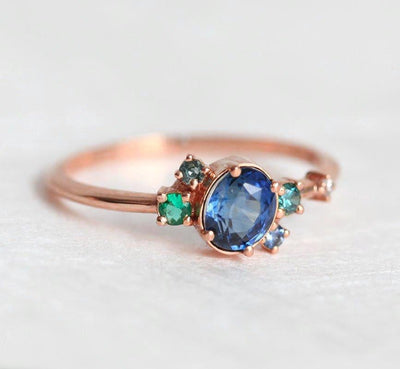 Blue oval sapphire ring with cluster diamonds and emeralds