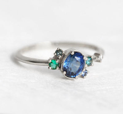 Blue oval sapphire ring with cluster diamonds and emeralds