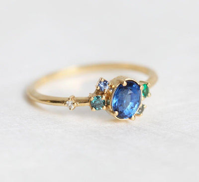 Blue oval sapphire ring with cluster diamonds and emeralds