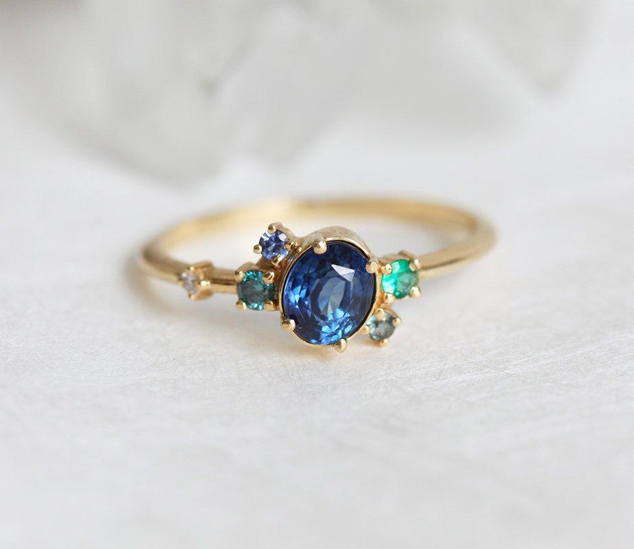 Blue oval sapphire ring with cluster diamonds and emeralds