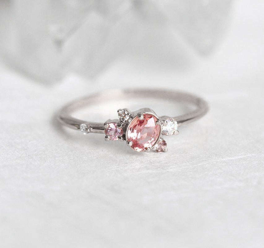 Oval-shaped pink-peach sapphire ring with diamond cluster