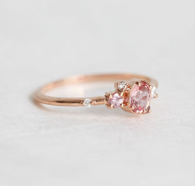 Oval-shaped pink-peach sapphire ring with diamond cluster