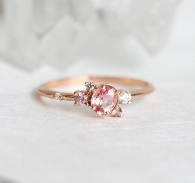 Oval-shaped pink-peach sapphire ring with diamond cluster