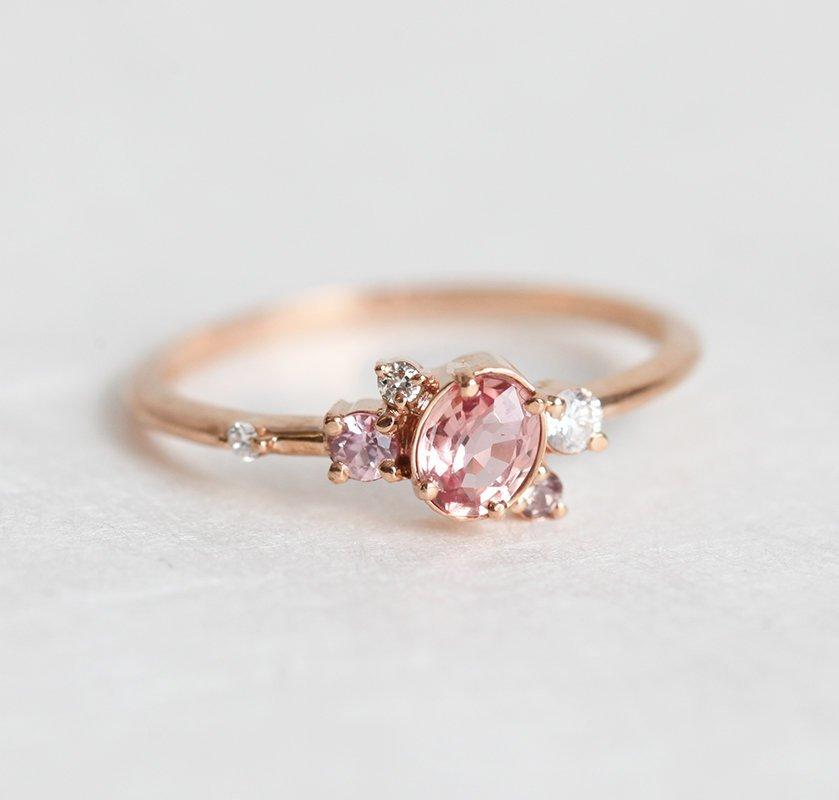 Oval-shaped pink-peach sapphire ring with diamond cluster