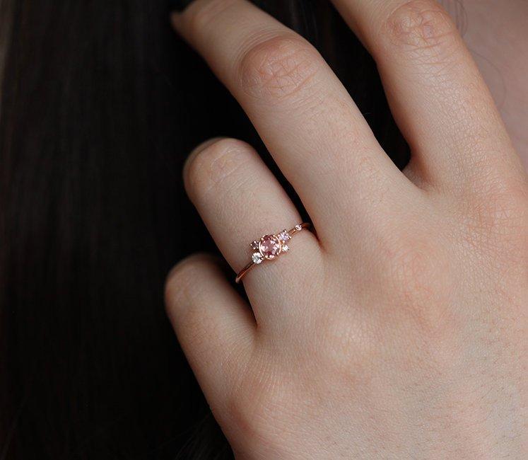 Oval-shaped pink-peach sapphire ring with diamond cluster