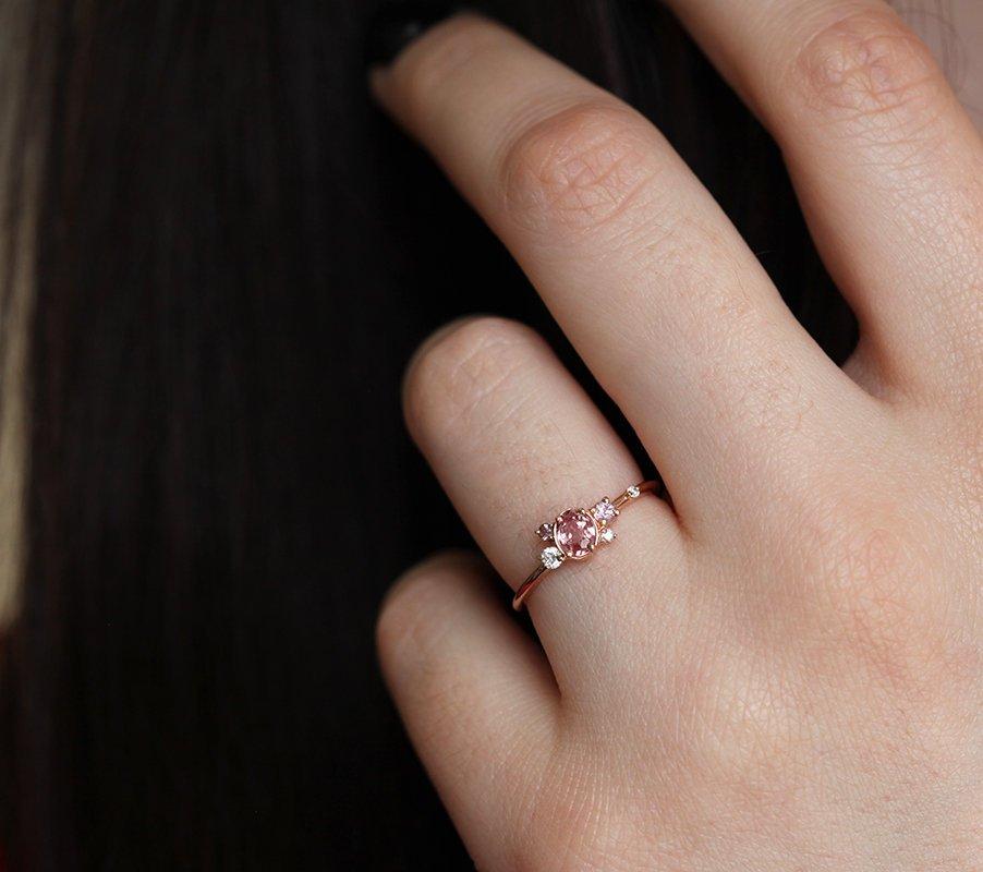 Oval-shaped pink-peach sapphire ring with diamond cluster