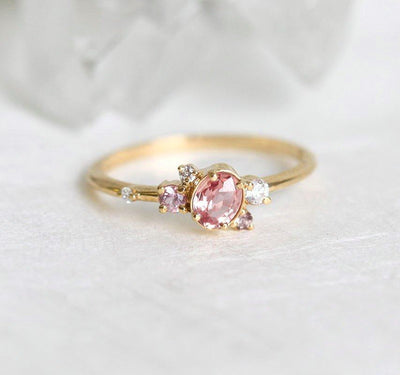 Oval-shaped pink-peach sapphire ring with diamond cluster