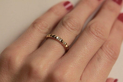 A gold ring with a pyramid textured design and a princess-cut white diamond