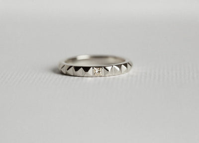 A gold ring with a pyramid textured design and a princess-cut white diamond