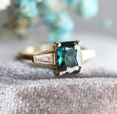 Emerald cut teal sapphire ring with baguette-shaped white diamond side stones