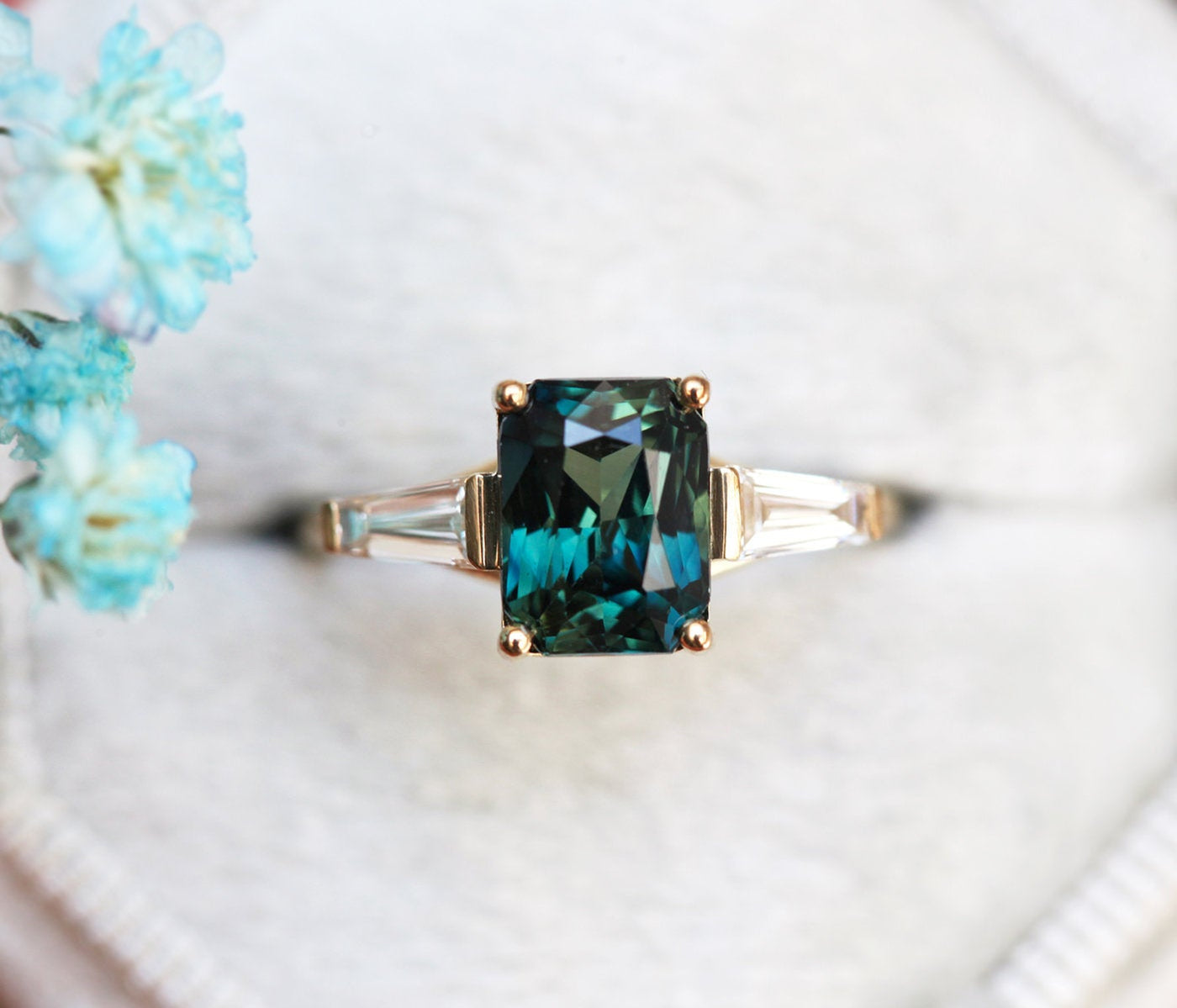 Emerald cut teal sapphire ring with baguette-shaped white diamond side stones