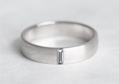 A silver baguette Emerald band ring with a diamond in the middle.