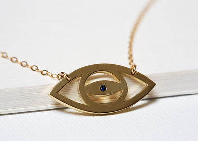 Gold eye silhouette necklace with round blue sapphire