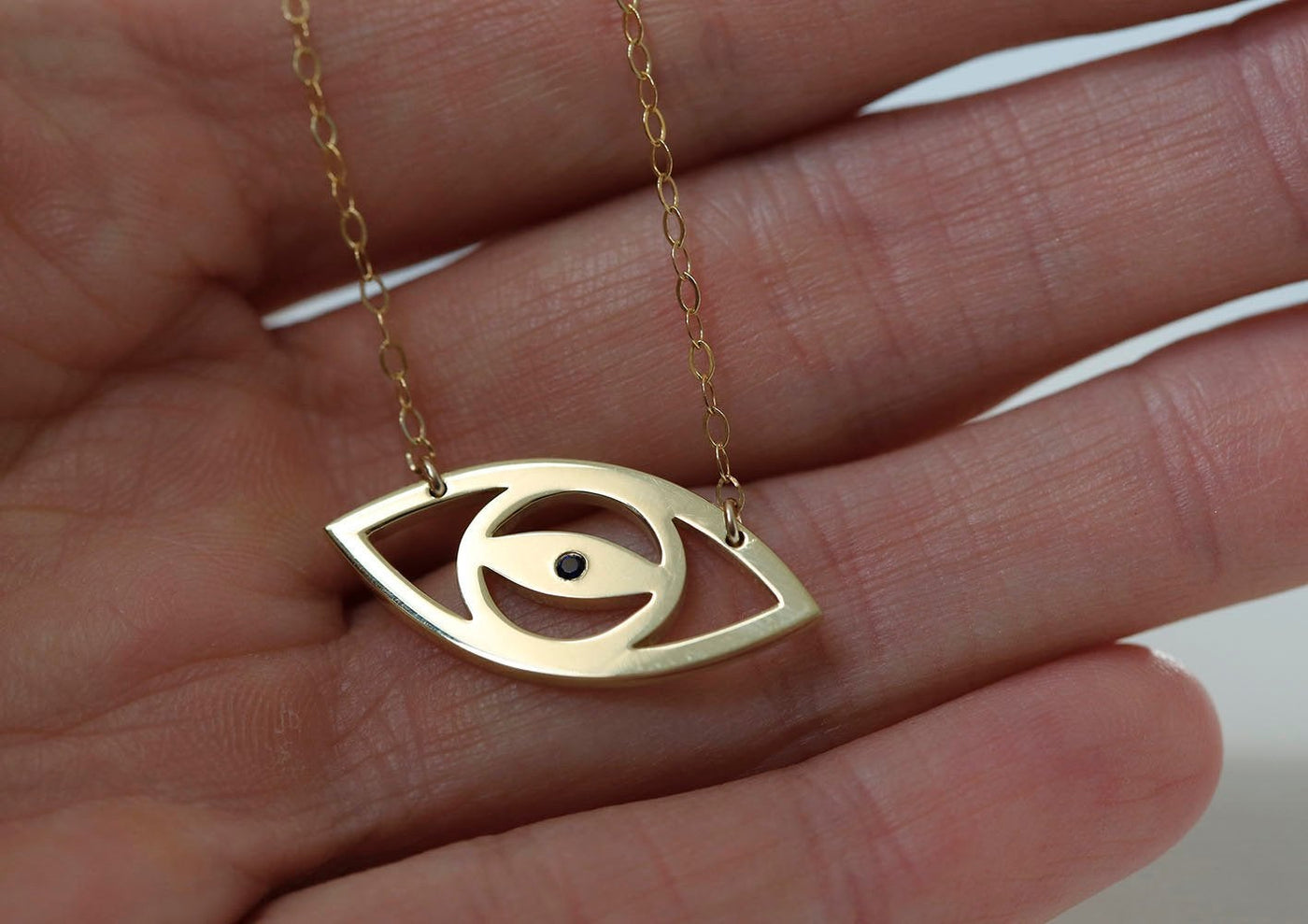 Gold eye silhouette necklace with round blue sapphire
