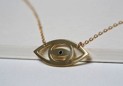 Gold eye silhouette necklace with round blue sapphire