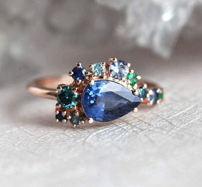 Pear-shaped blue sapphire cluster ring with diamond, topaz and emerald side stones