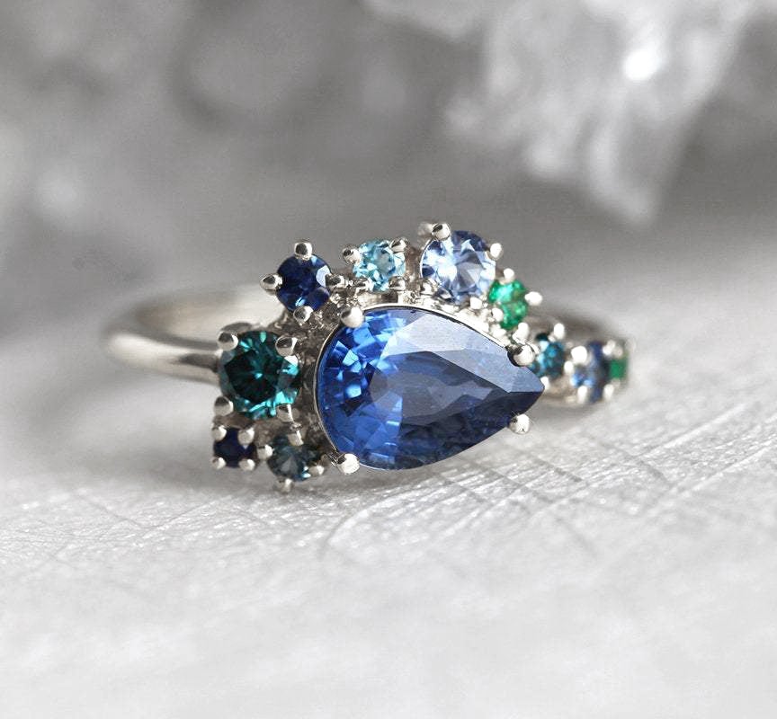 Pear-shaped blue sapphire cluster ring with diamond, topaz and emerald side stones