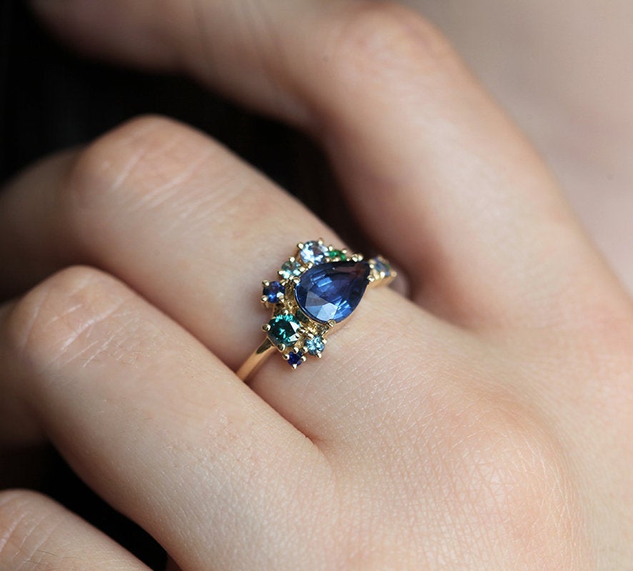 Pear-shaped blue sapphire cluster ring with diamond, topaz and emerald side stones