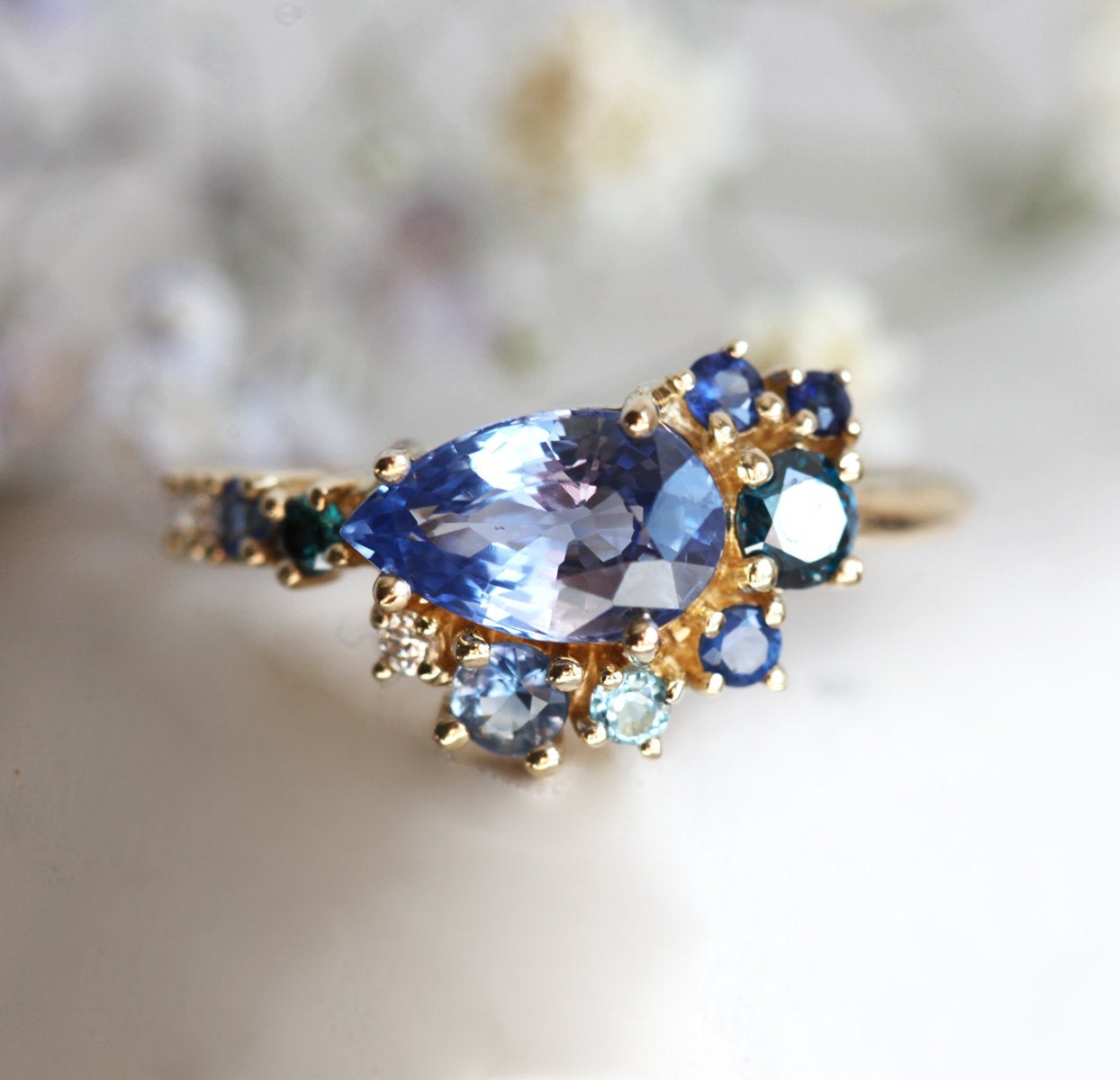 Pear-shaped blue sapphire cluster ring with diamond, topaz and emerald side stones