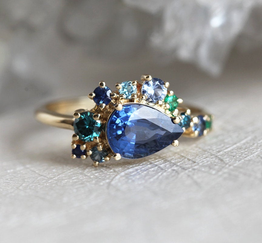 Pear-shaped blue sapphire cluster ring with diamond, topaz and emerald side stones