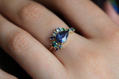 Pear-shaped blue sapphire cluster ring with diamond, topaz and emerald side stones