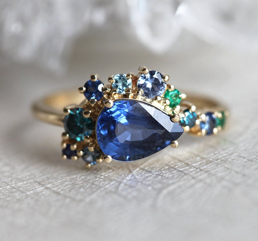 Pear-shaped blue sapphire cluster ring with diamond, topaz and emerald side stones