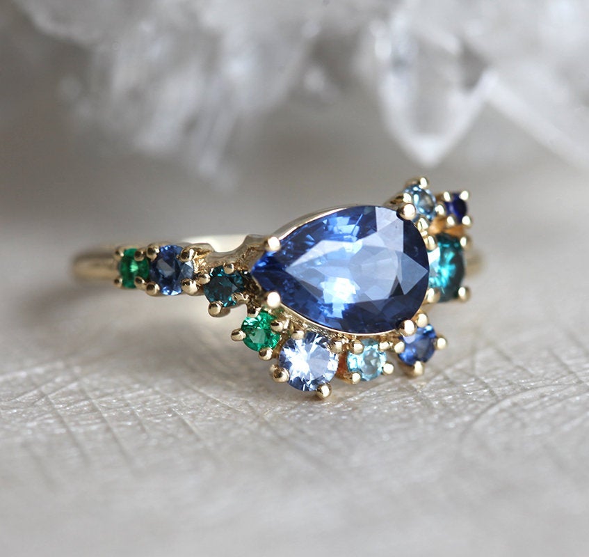 Pear-shaped blue sapphire cluster ring with diamond, topaz and emerald side stones