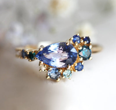 Pear-shaped blue sapphire cluster ring with diamond, topaz and emerald side stones