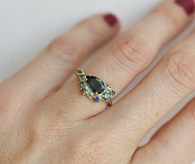 Pear-shaped teal sapphire cluster ring with diamond, topaz and emerald side stones