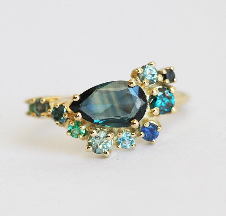 Pear-shaped teal sapphire cluster ring with diamond, topaz and emerald side stones