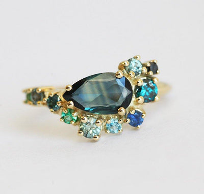 Pear-shaped teal sapphire cluster ring with diamond, topaz and emerald side stones