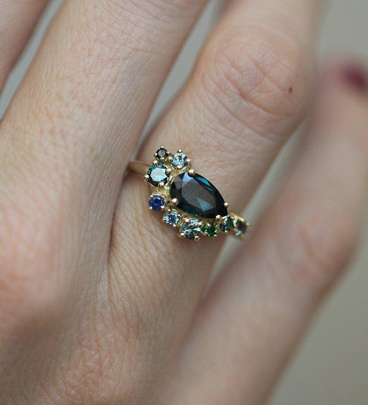 Pear-shaped teal sapphire cluster ring with diamond, topaz and emerald side stones