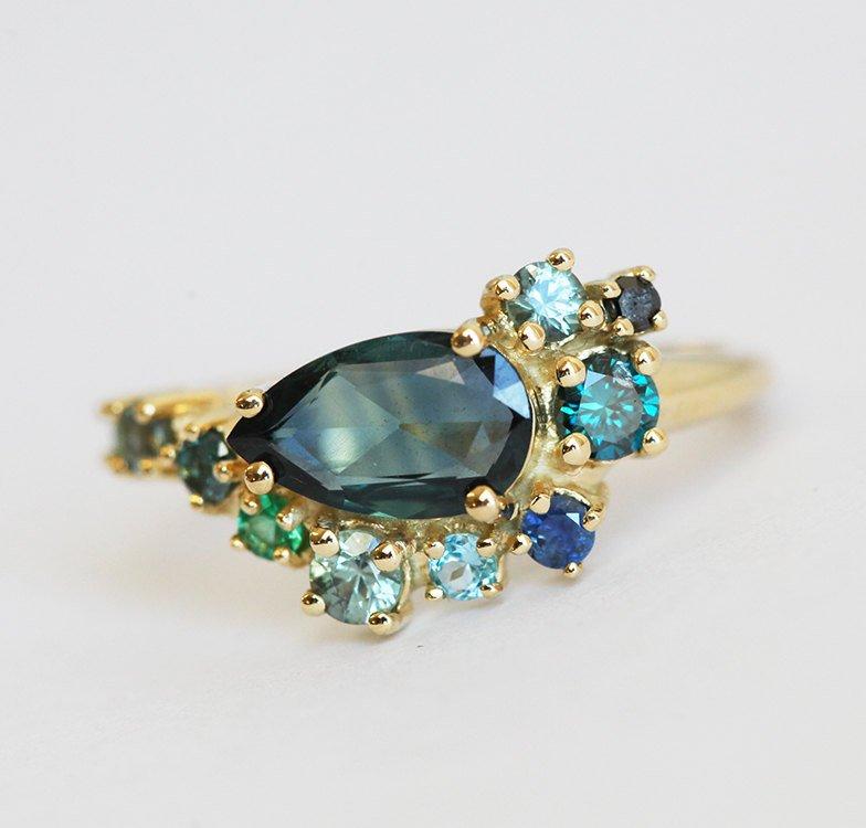 Pear-shaped teal sapphire cluster ring with diamond, topaz and emerald side stones