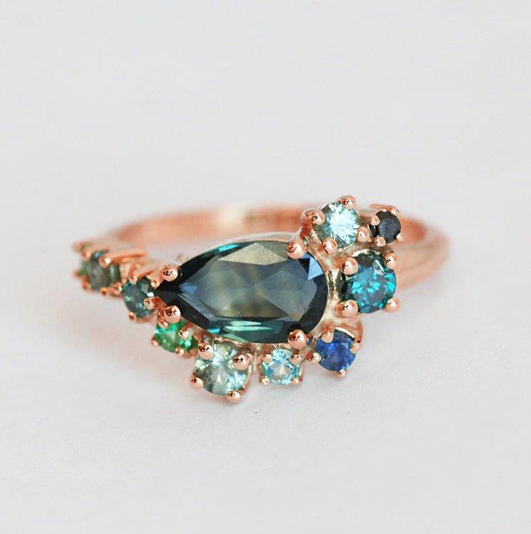 Pear-shaped teal sapphire cluster ring with diamond, topaz and emerald side stones