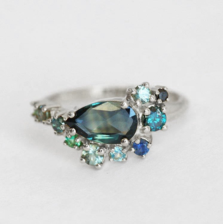 Pear-shaped teal sapphire cluster ring with diamond, topaz and emerald side stones