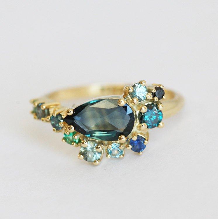 Pear-shaped teal sapphire cluster ring with diamond, topaz and emerald side stones