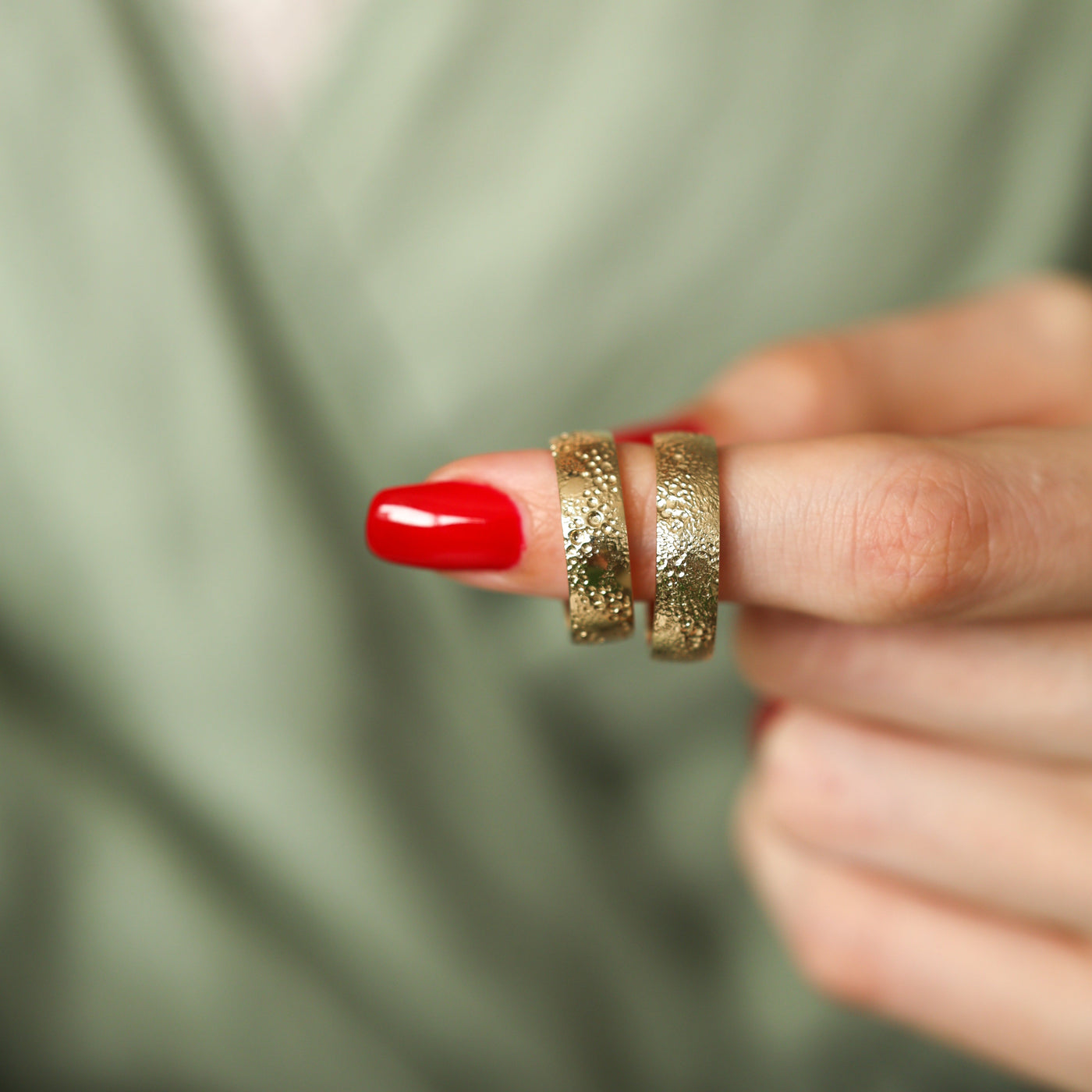 Textured gold wedding band on a finger with red nails and gold rings. Unisex twist design in 14k and 18k gold.