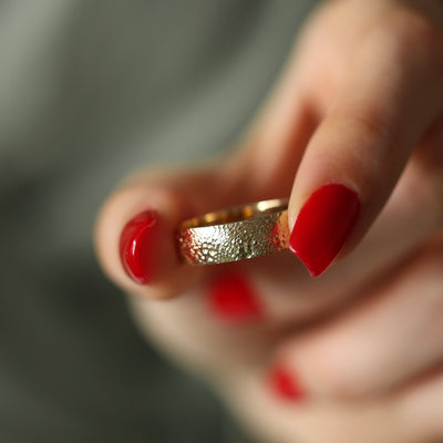 A textured gold wedding band held in a hand, showcasing intricate details.