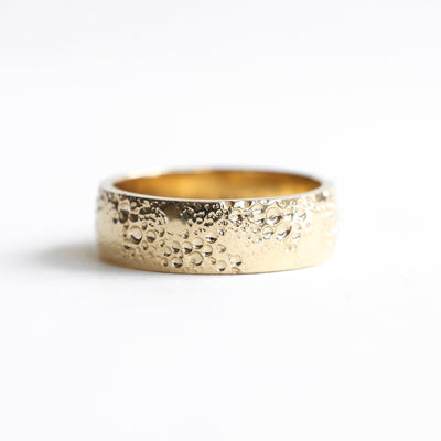 Textured gold wedding band with water droplets, showcasing a unique twist design. Unisex, available in various metals and widths.