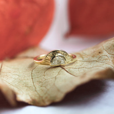 Unique 14k gold ring with a round white diamond in a half moon shape and sun rays engraved into the ring texture