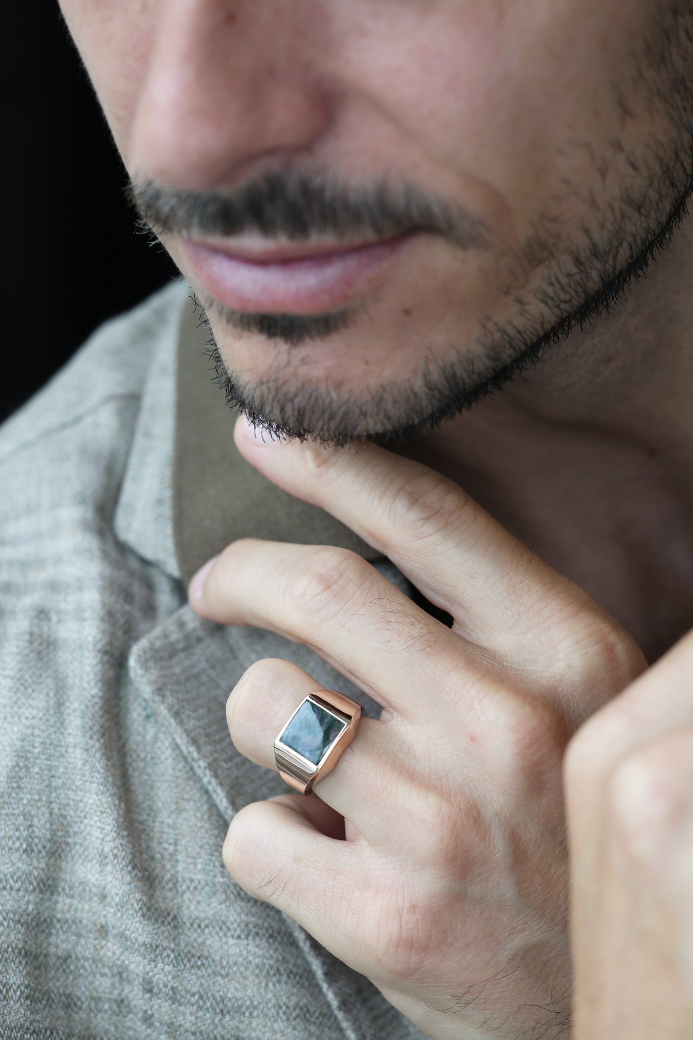 Close-up of a man's face wearing a Moss Agate Signet Ring in gold and platinum.