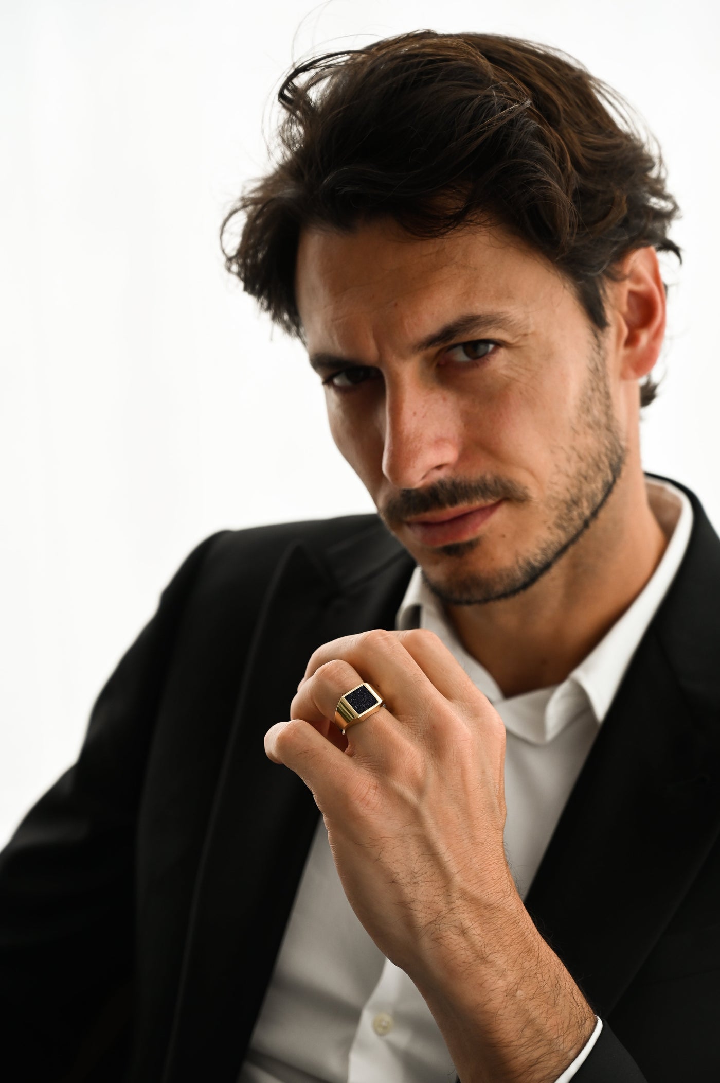 A man in a suit showcasing the Jazz Goldstone Signet Ring, a men's gold and platinum design with a goldstone gemstone.